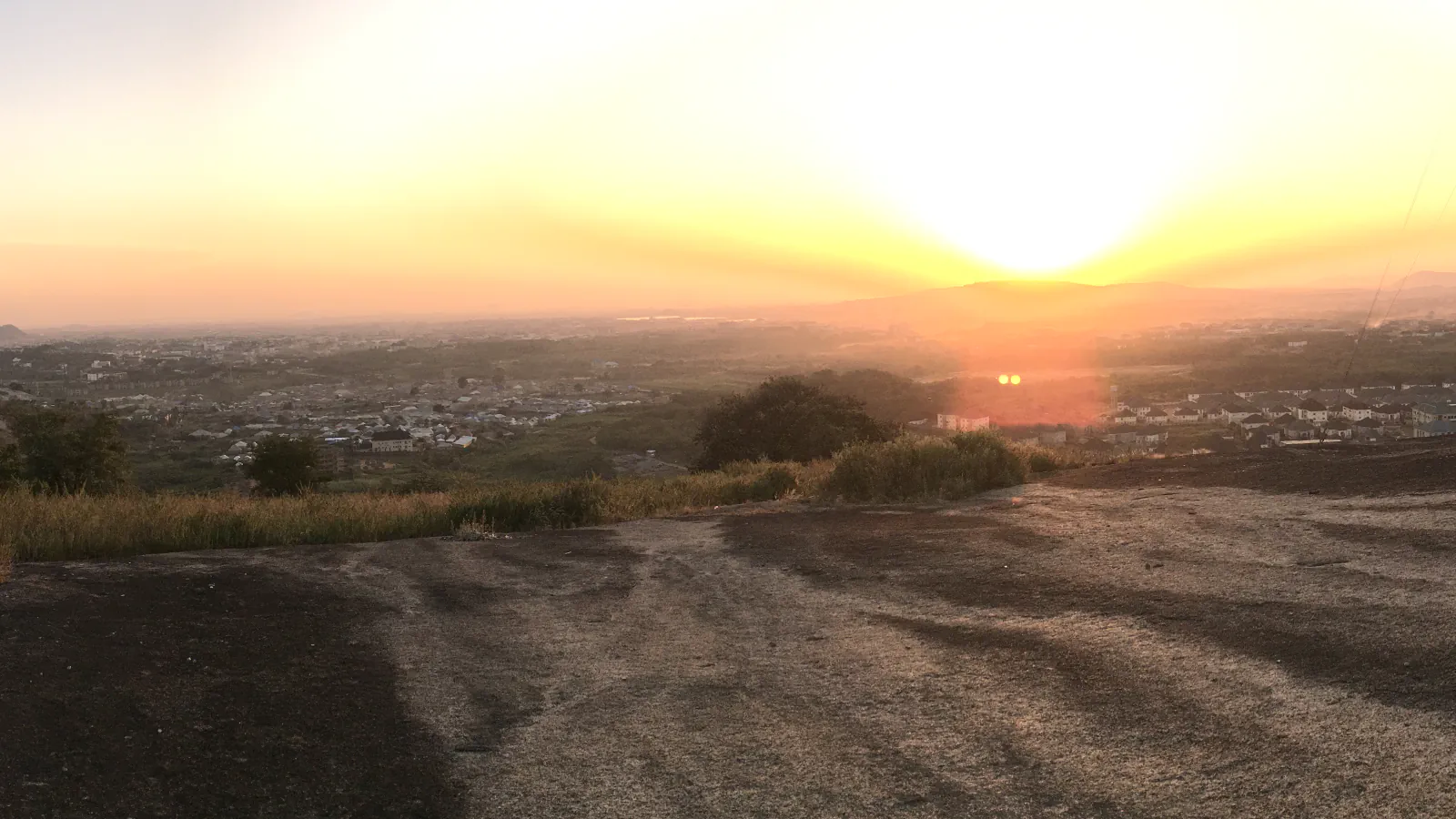 Sun setting over the hazy houses and distant hills of Abuja, seen from a rocky hilltop