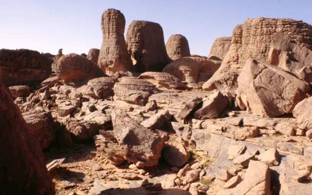 Weathered sandstone towers above broken slabs under a clear sky on the Tassili n’Ajjer plateau.