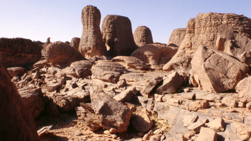 Weathered sandstone towers above broken slabs under a clear sky on the Tassili n’Ajjer plateau.