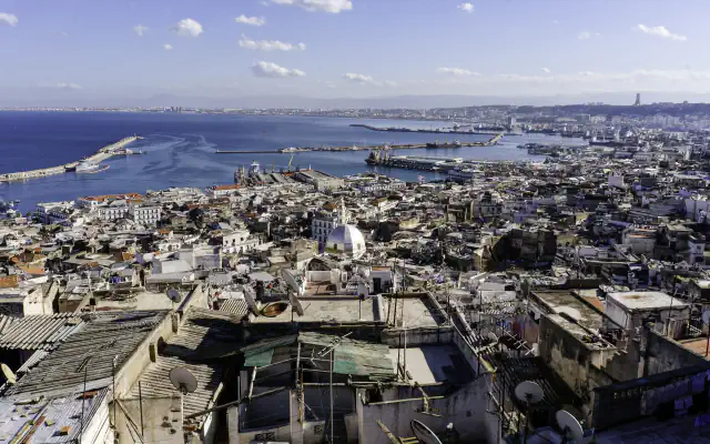 Flat roof terraces of the Casbah in the foreground, a white dome among the dense houses of the lower town, and the harbour moles and the Bay of Algiers beyond