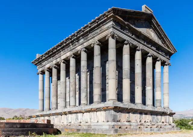 Ionic columns and pediment of the Garni temple under a clear blue sky, with hills behind