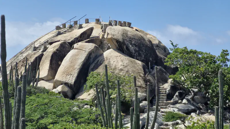 Rounded pale boulders at Casibari, Aruba, with stone steps and railings climbing to the top, columnar cacti in front and blue sky behind