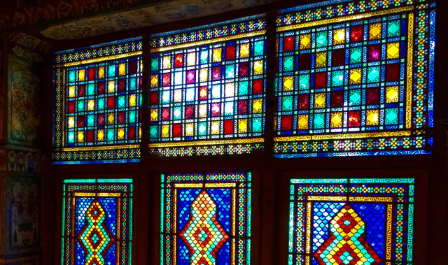 Six wooden-framed windows glow with small panes of red, yellow, turquoise and deep blue glass, the upper three in square grids and the lower three with diamond-shaped medallions at their centre