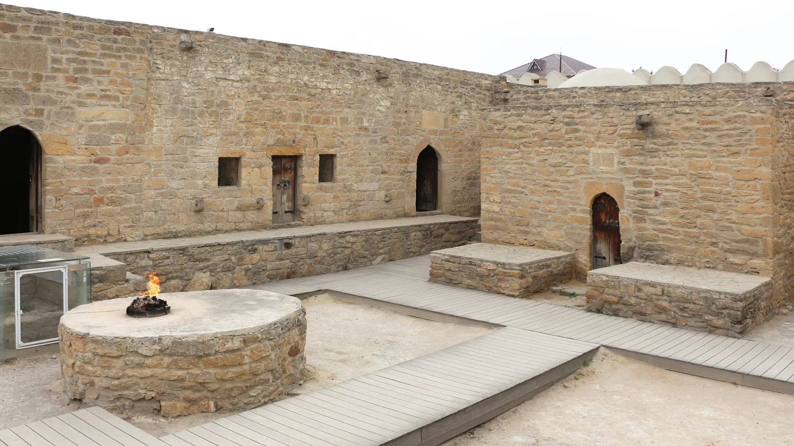 Stone-walled courtyard of the Ateshgah at Surakhany with a small flame on a round stone platform and wooden walkways