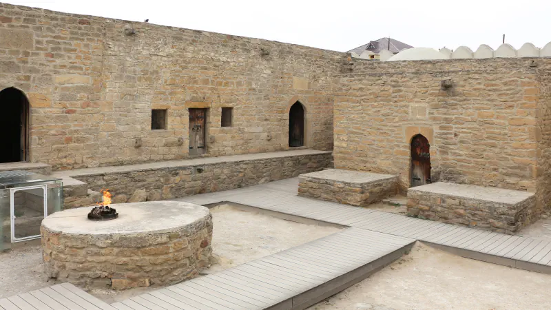 Stone-walled courtyard of the Ateshgah at Surakhany with a small flame on a round stone platform and wooden walkways