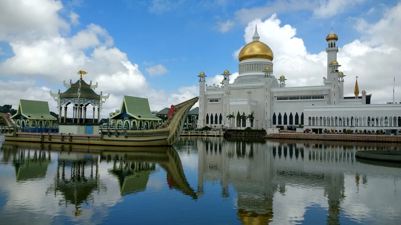 A replica royal barge with roofed pavilions on the lagoon, with the golden-domed Omar Ali Saifuddien Mosque behind it