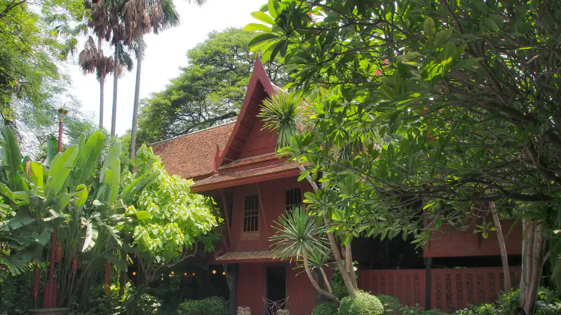 Red-brown timber house with a pitched roof among dense garden trees in Bangkok