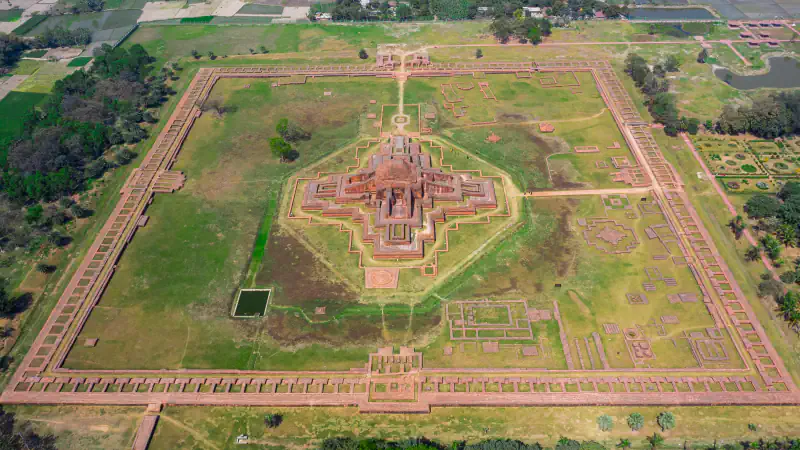 Aerial view of Somapura Mahavihara at Paharpur: a square enclosure of monastery cells around a cross-shaped central shrine, with low ruins across a grassy courtyard