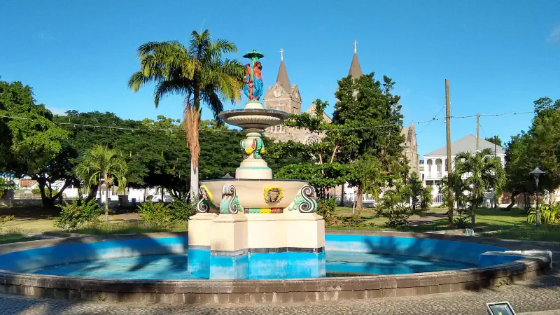 Colourful fountain within a blue basin at Independence Square in Basseterre, with palms and church towers behind