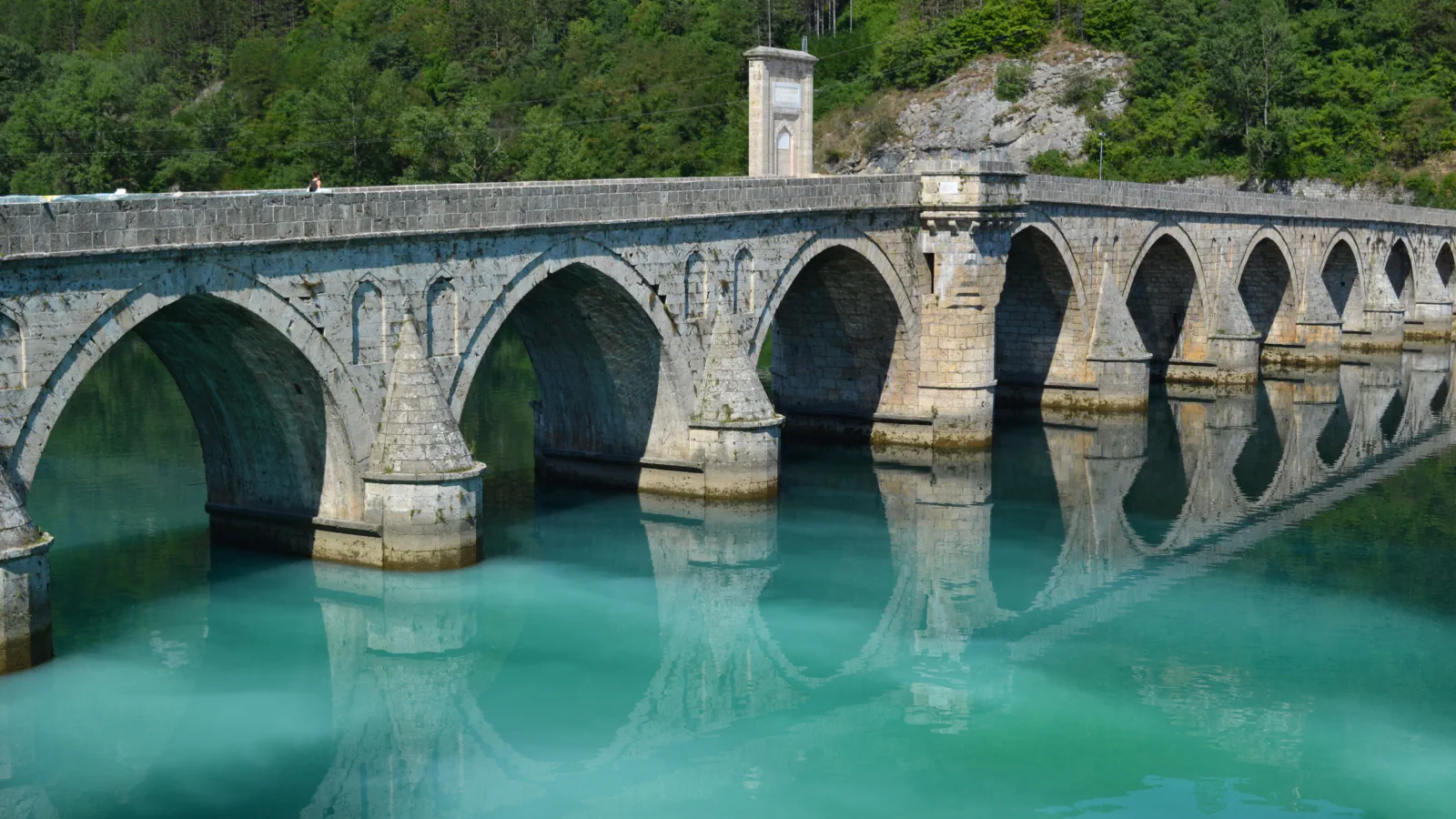 Stone arches of the Mehmed Paša Sokolović Bridge over the pale green Drina, with pointed pier heads and the arches reflected in the water