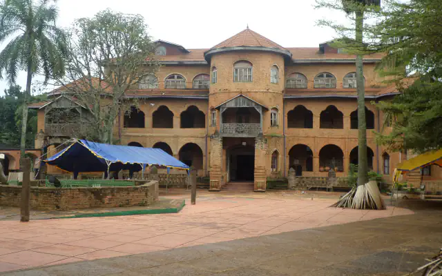Front of a brick palace with a round central tower under a pointed reddish roof, two levels of arched arcades and an open paved courtyard with a blue tent on the left