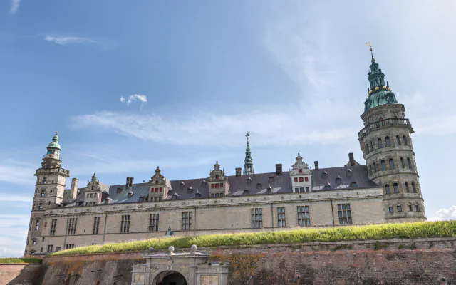 Sandstone wing of Kronborg Castle with towers and green copper spires rising above a grass-topped brick rampart and gateway