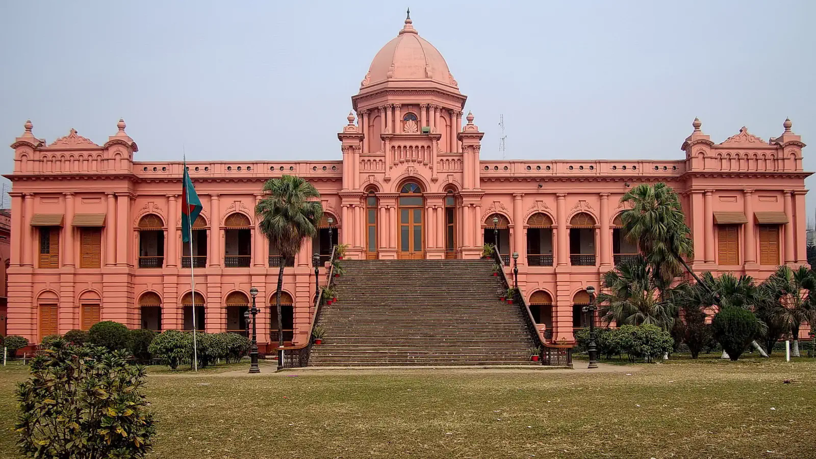 Pink Ahsan Manzil façade and dome framed by trees in Dhaka