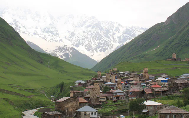 Svan tower houses and village buildings at Ushguli above a stream, with snow-covered peaks behind