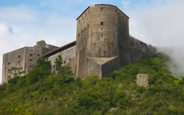 Stone walls and a broad tower rise above a green hillside; mist drifts across the right side.