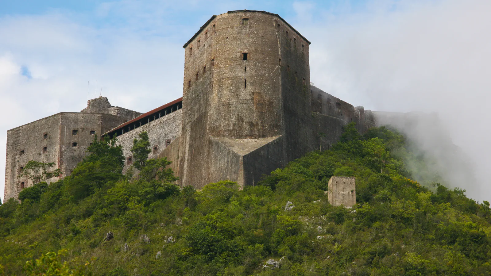 Stone walls and a broad tower rise above a green hillside; mist drifts across the right side.