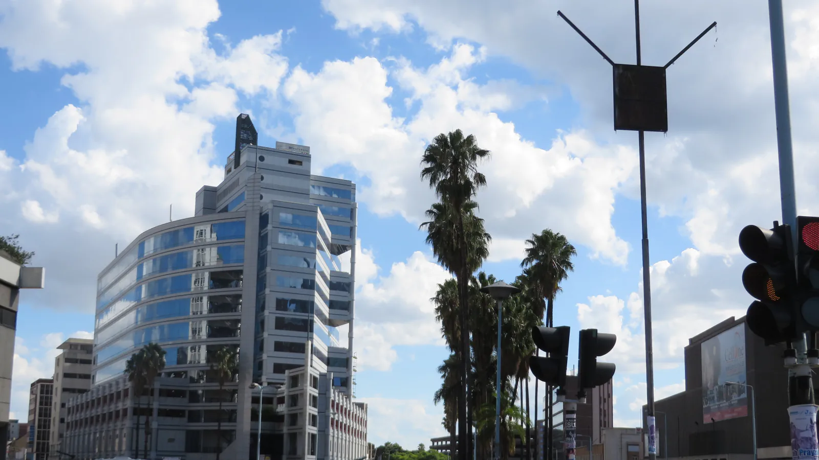 Glass-fronted building and tall palm trees along a Harare street beneath a partly cloudy sky