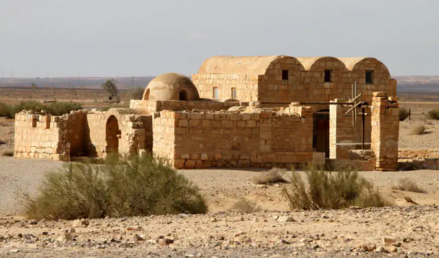 Low stone bathhouse of Quseir Amra in open stony desert, with three barrel-vaulted roofs, a small dome and a wooden frame beside the entrance