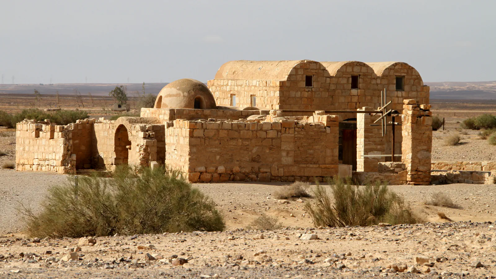 Low stone bathhouse of Quseir Amra in open stony desert, with three barrel-vaulted roofs, a small dome and a wooden frame beside the entrance