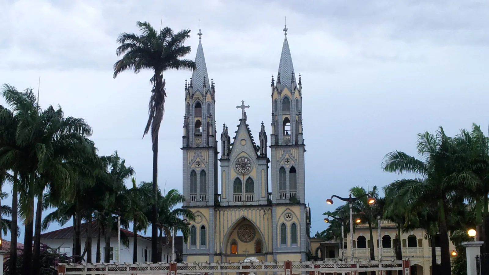 The twin-towered façade of the Cathedral of Santa Isabel in Malabo between palm trees under a cloudy sky