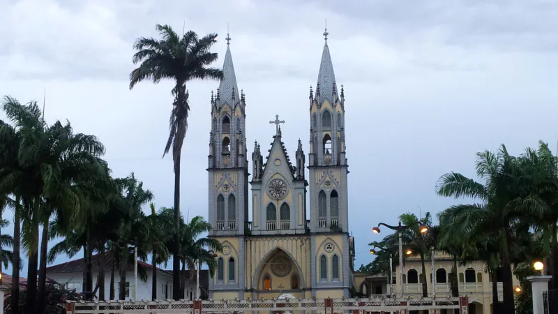 The twin-towered façade of the Cathedral of Santa Isabel in Malabo between palm trees under a cloudy sky