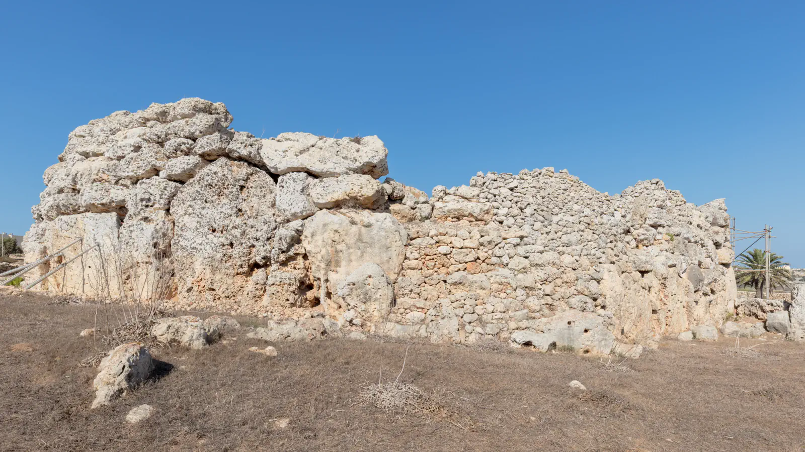 Weathered limestone wall of the Ġgantija temples, with large blocks on the left and smaller stones on the right, under a clear sky