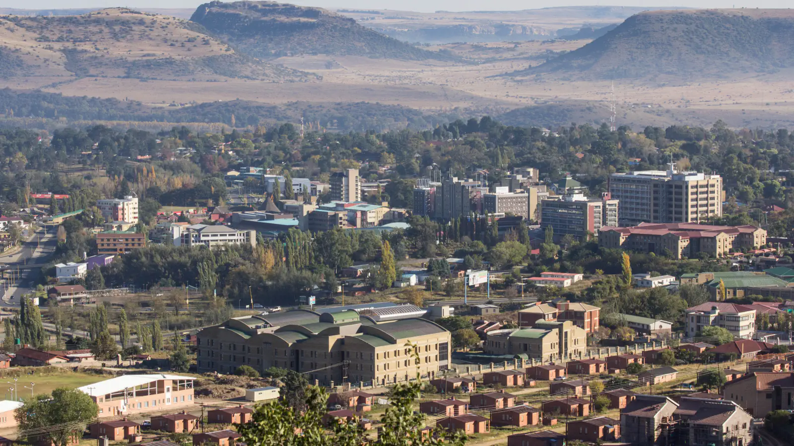 Strehe, drevesa in oddaljeni hribi na širokem pogledu na mesto Maseru