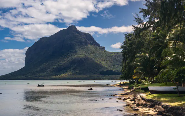 Le Morne Brabant rises beyond a shallow lagoon, with boats moored along the palm-lined shore.