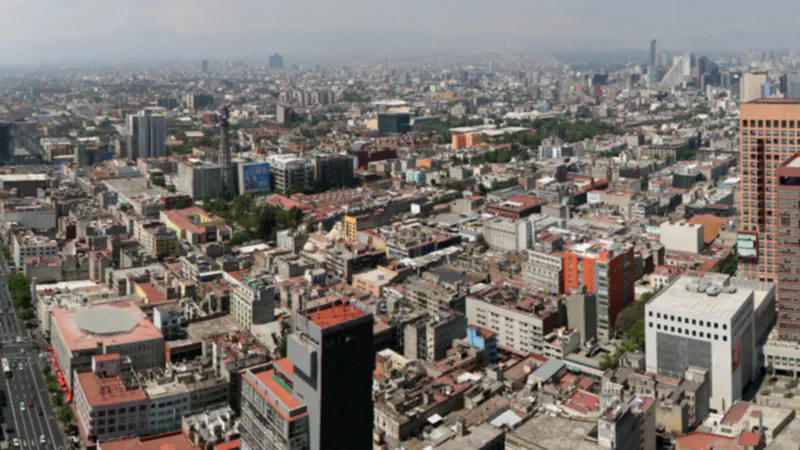 High-angle panorama across Mexico City’s dense urban fabric, with buildings and towers beneath a hazy sky