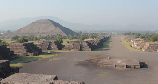 Wide Avenue of the Dead at Teotihuacan on a hazy day, with the Pyramid of the Sun at left and low stepped platforms along the avenue
