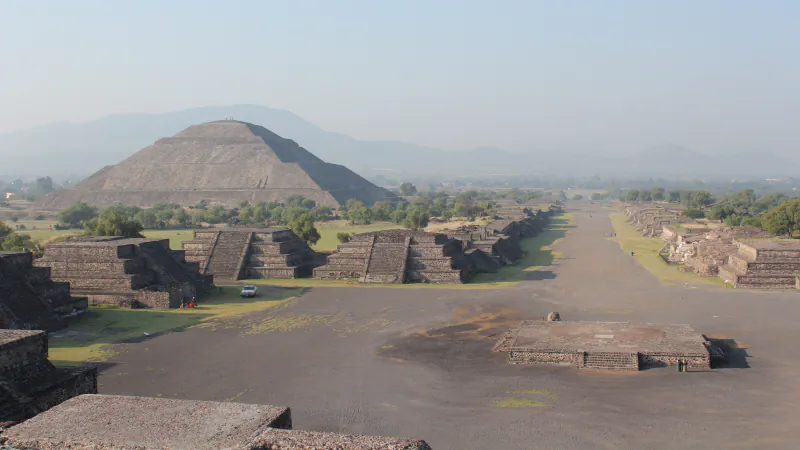 Wide Avenue of the Dead at Teotihuacan on a hazy day, with the Pyramid of the Sun at left and low stepped platforms along the avenue