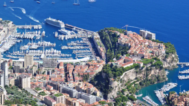 Rock of Monaco above the harbour, with clustered buildings and boats seen from a distant hillside