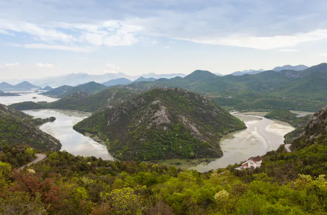 A river winds in a wide bend between green hills, with lake water and layered mountains in the distance