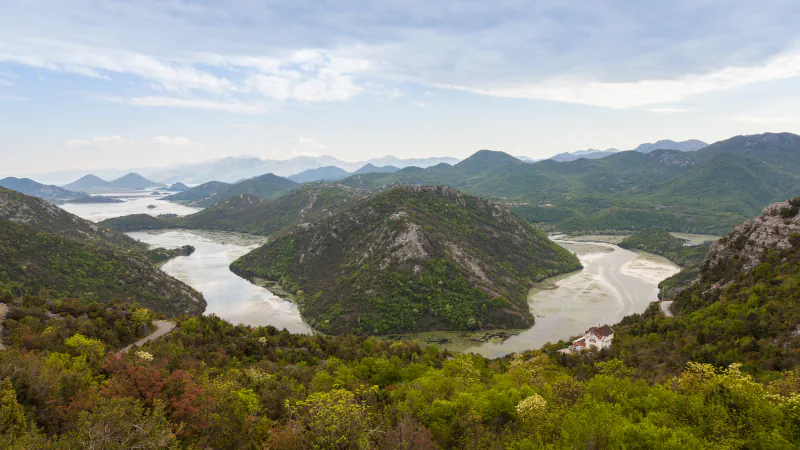 A river winds in a wide bend between green hills, with lake water and layered mountains in the distance