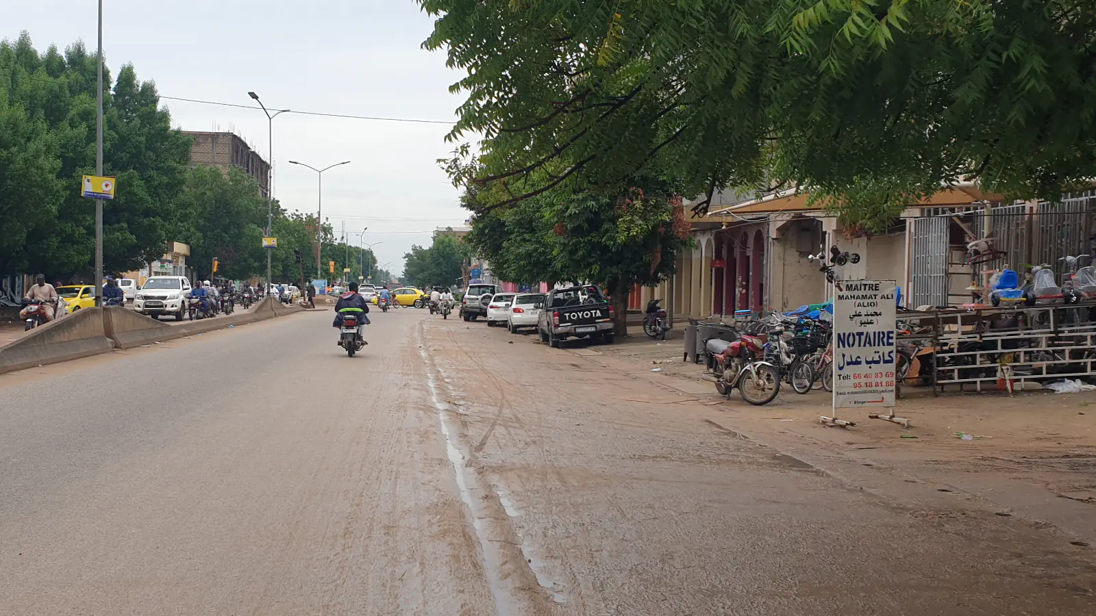 Široka ulica v mestu N’Djamena z nizkimi stavbami in oddaljenim prometom