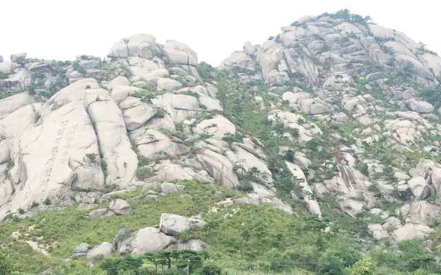 Pale rounded granite slopes dotted with pines under a hazy sky, with Korean characters carved into one rock face