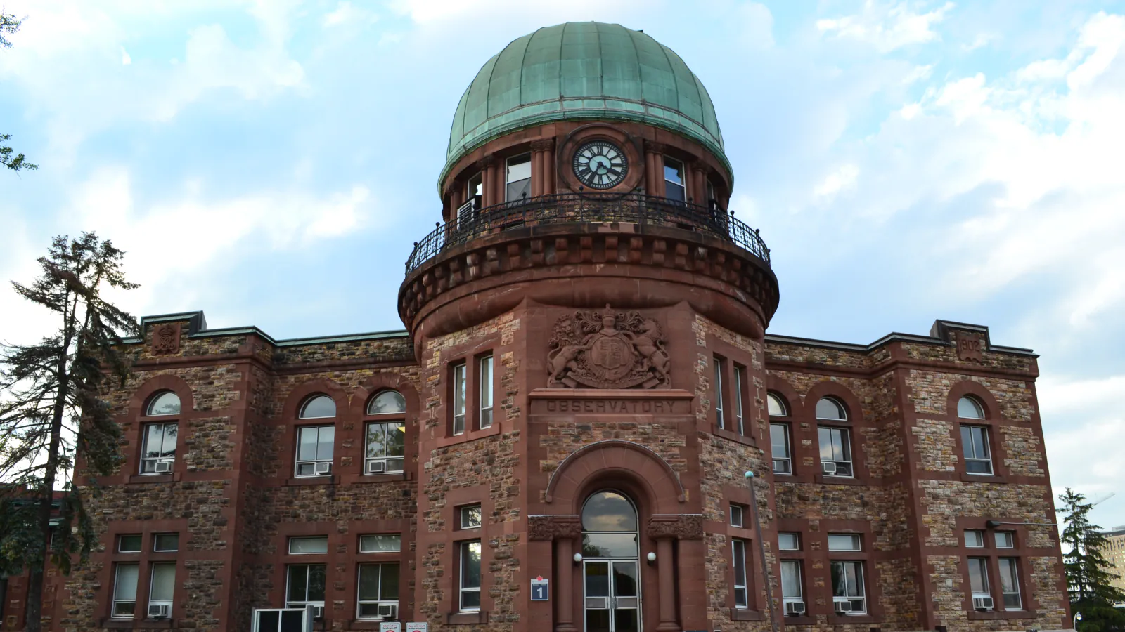 The stone front of the Dominion Observatory in Ottawa, with its green copper dome and clock, under a cloudy sky