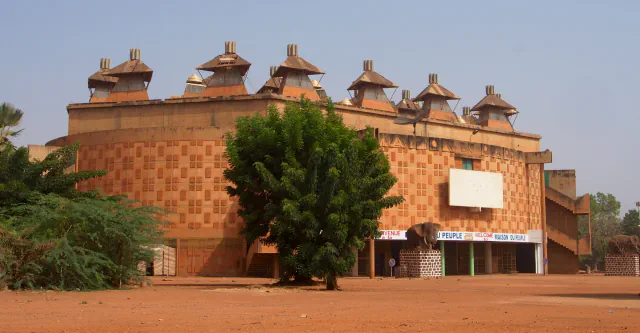 The circular Maison du Peuple with pyramid-shaped roof lanterns, seen across red earth