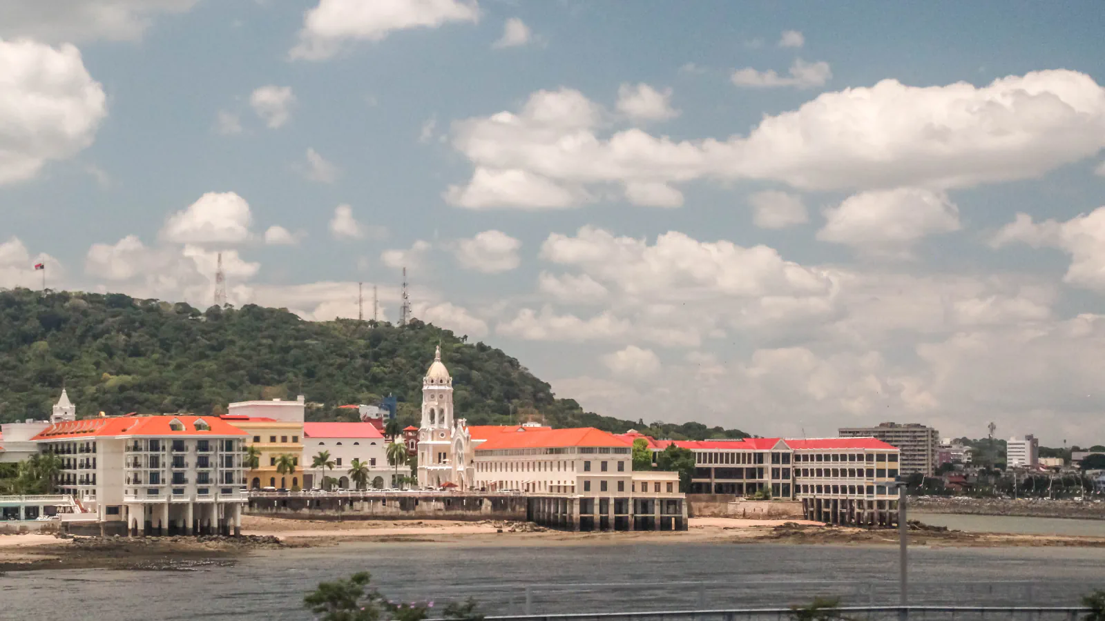 Waterfront buildings and a white tower in Casco Viejo, Panama City, with a forested hill behind