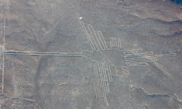 Aerial view of the hummingbird geoglyph, a thin pale line drawing on the grey-brown ground of the Nasca plain