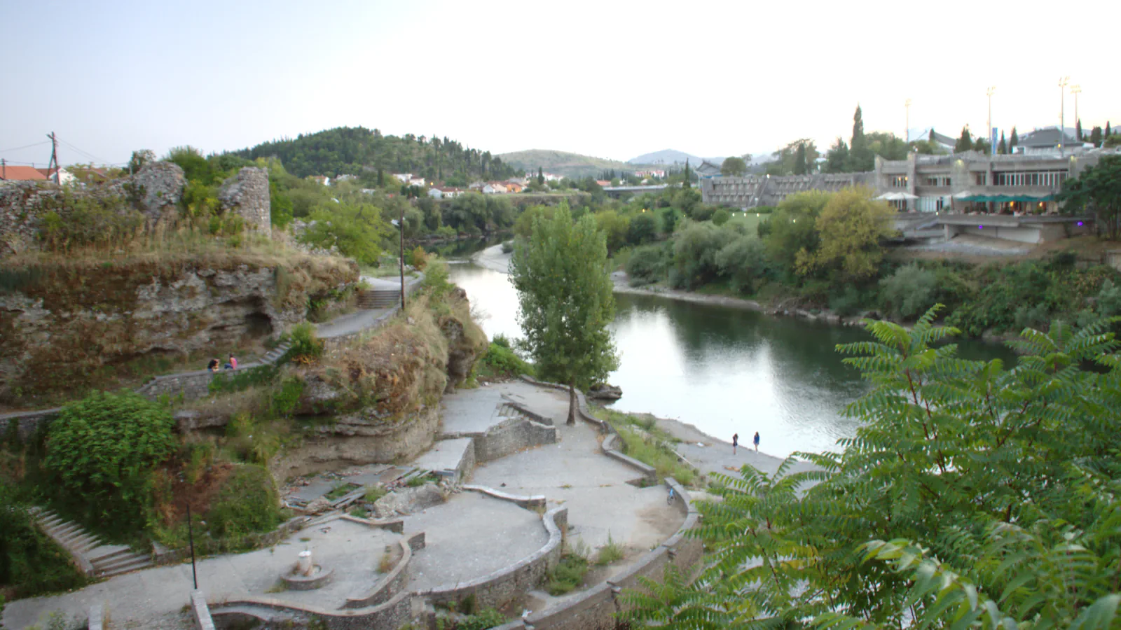 Morača riverbank in Podgorica with stone terraces, trees and hills beyond