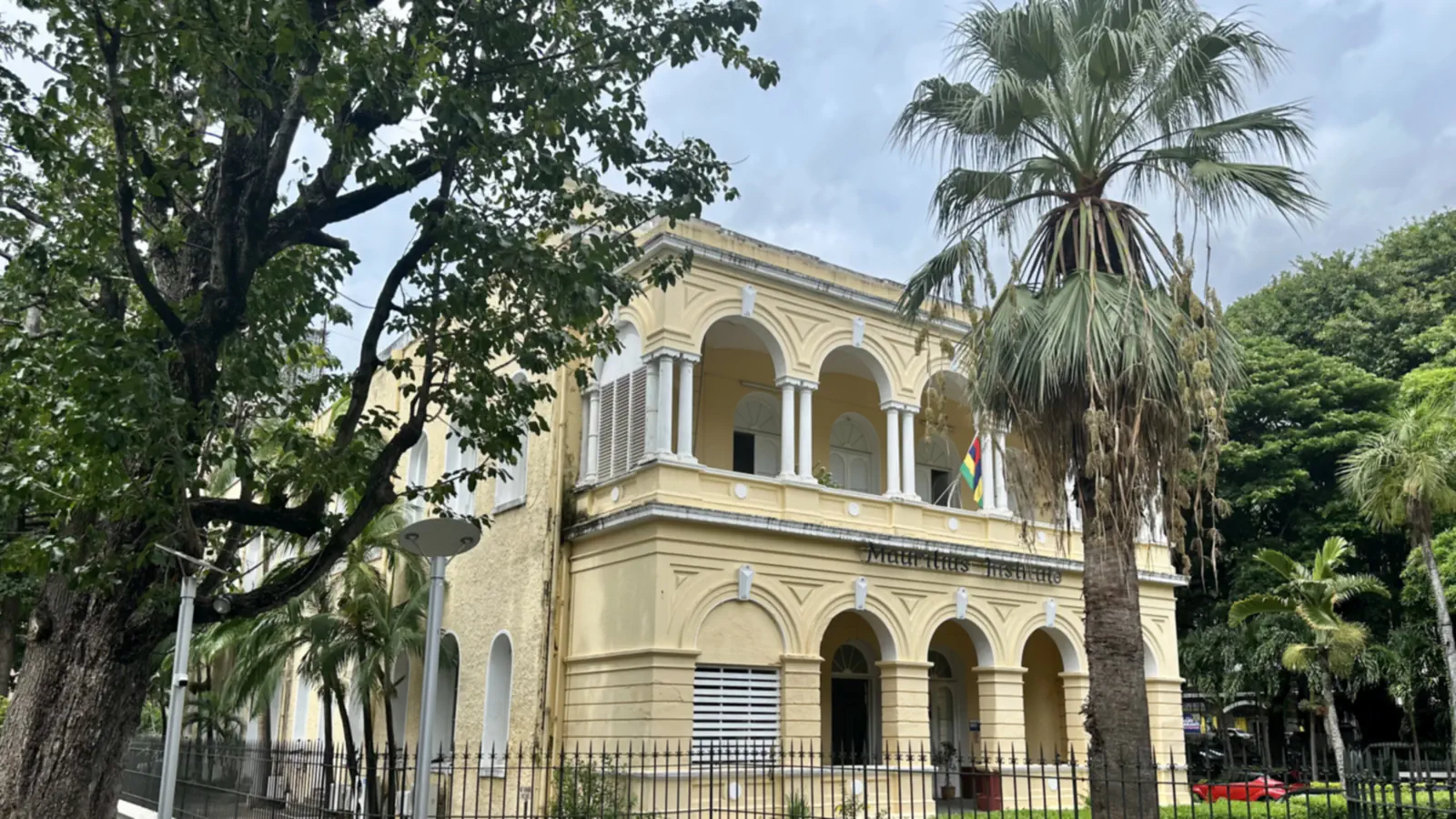 Cream arched façade and balcony of the Natural History Museum in Port Louis, framed by trees