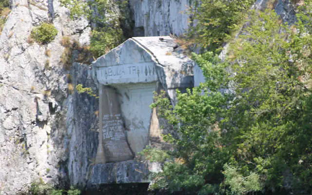 Trajan’s Tablet, a Roman inscription cut into the rock wall of the Đerdap gorge, seen from the Danube with green trees on the bank