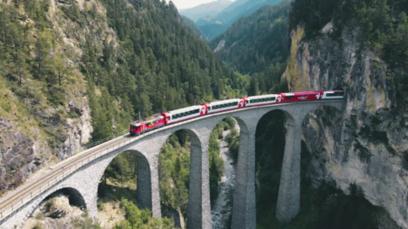 Rdeče-beli potniški vlak na kamnitem ločnem viaduktu Landwasser nad gozdnato sotesko