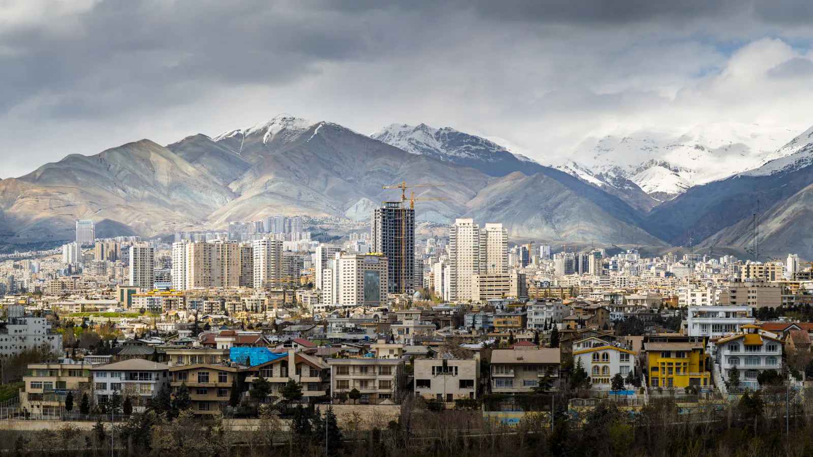 A dense Tehran skyline below the snow-covered Alborz mountains