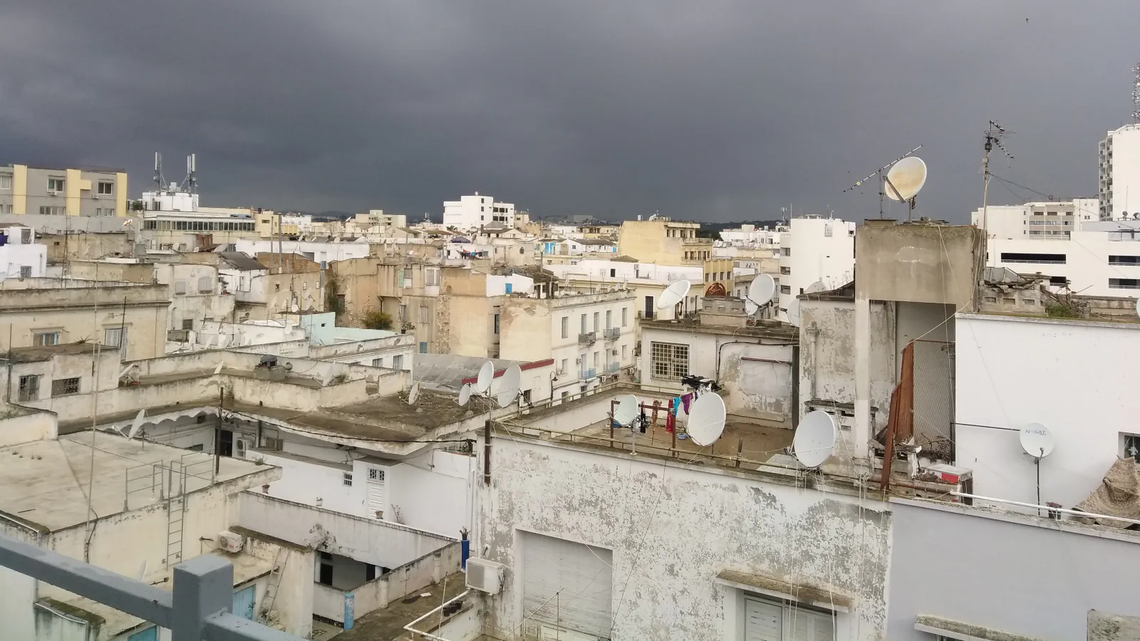 Rooftops, buildings and satellite dishes in Tunis beneath dark storm clouds.