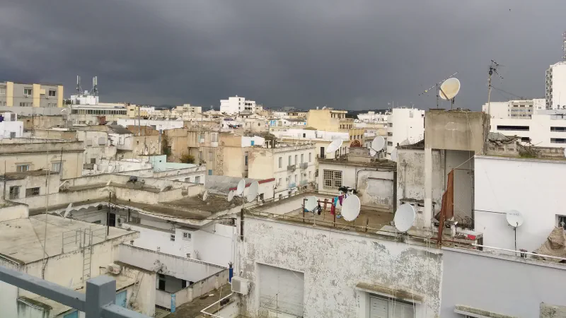 Strehe, stavbe in satelitske antene v Tunisu pod temnimi nevihtnimi oblaki.