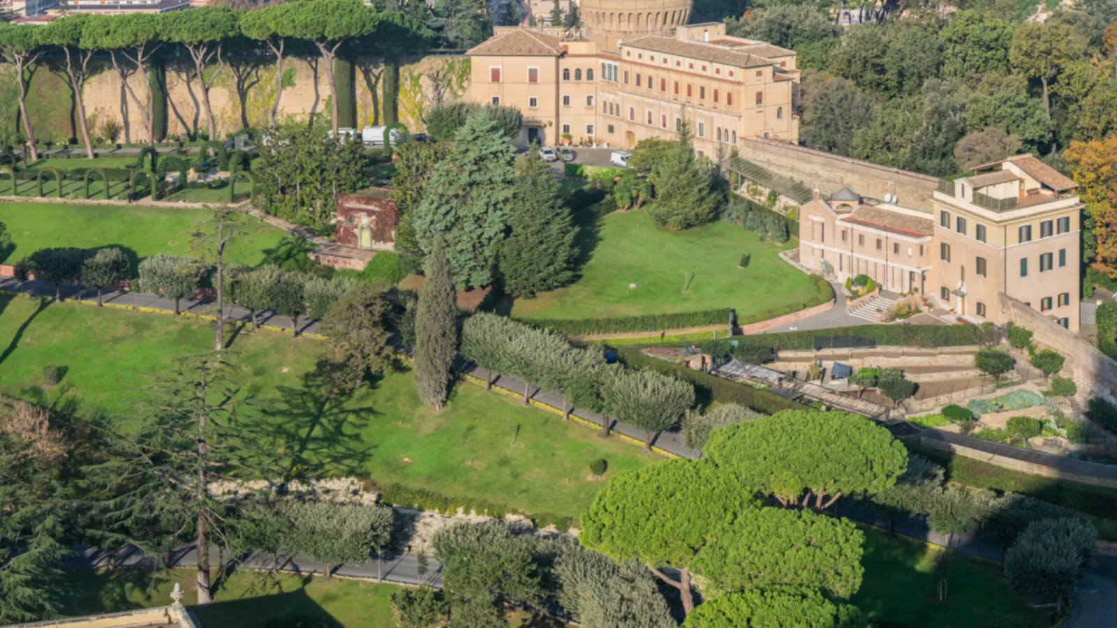 Paths and lawns in the Vatican Gardens, among trees and garden buildings.