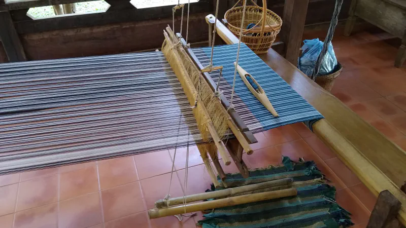 Lesene statve z modro-sivimi nitmi osnove in čolničkom na ploščicah, nad njimi viseča košara.