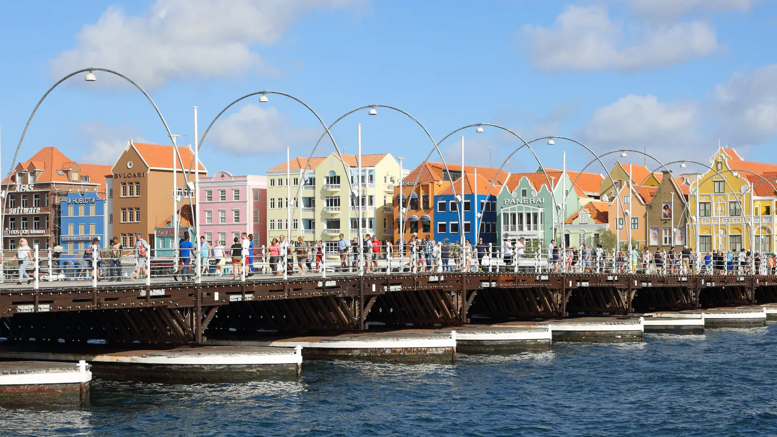 Pedestrians on the floating Queen Emma Bridge with Willemstad’s colourful waterfront behind